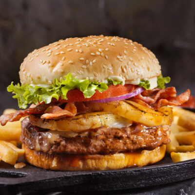 A burger with lettuce tomato and pineapple with french fries on the side.
