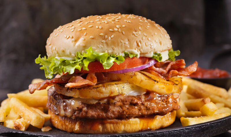 A burger with lettuce tomato and pineapple with french fries on the side.