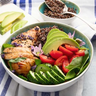 Quinoa bowl topped with chicken, avocado, tomatoes, and cucumbers