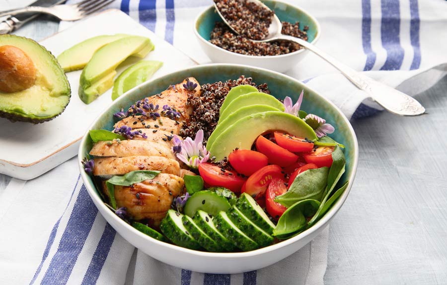 Quinoa bowl topped with chicken, avocado, tomatoes, and cucumbers