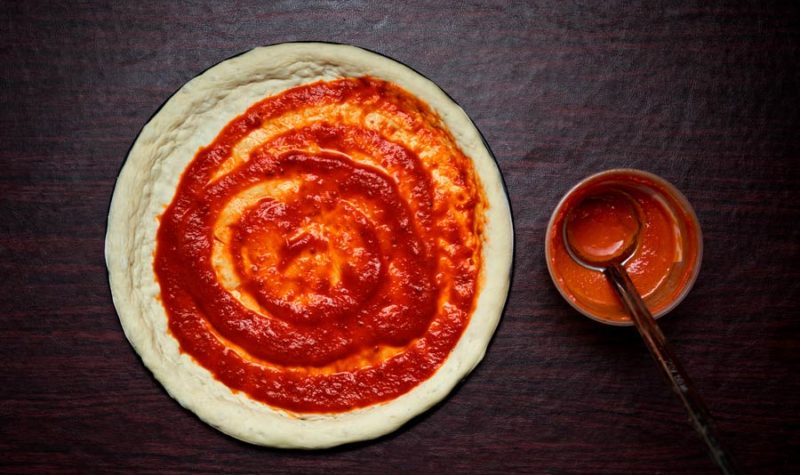 An overhead photo of pizza crust topped with sauce