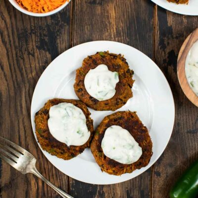 A white plate with 3 black bean cakes topped with a jalapeno sour cream.