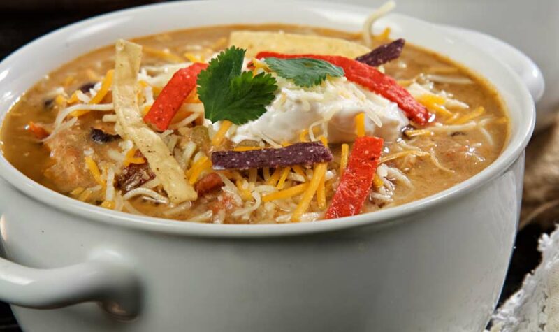 A bowl of chicken enchilada soup topped with cheese and tortilla strips.