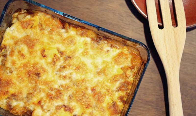 A glass baking dish willed with a cheesy casserole and a wooden spoon on the side.