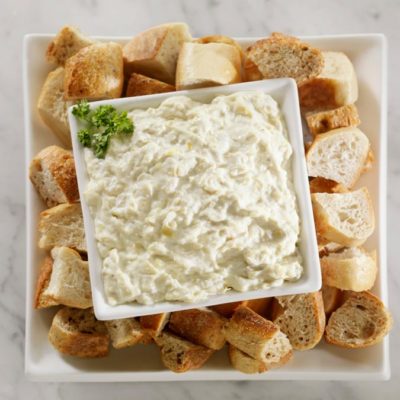 A platter with crackers and a bowl of artichoke dip.