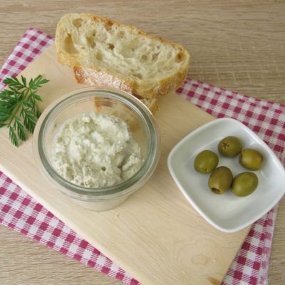 A glass bowl filled with cream cheese dip and a side of green olives and bread.