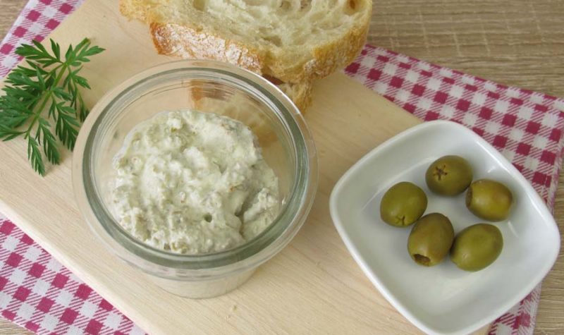A glass bowl filled with cream cheese dip and a side of green olives and bread.