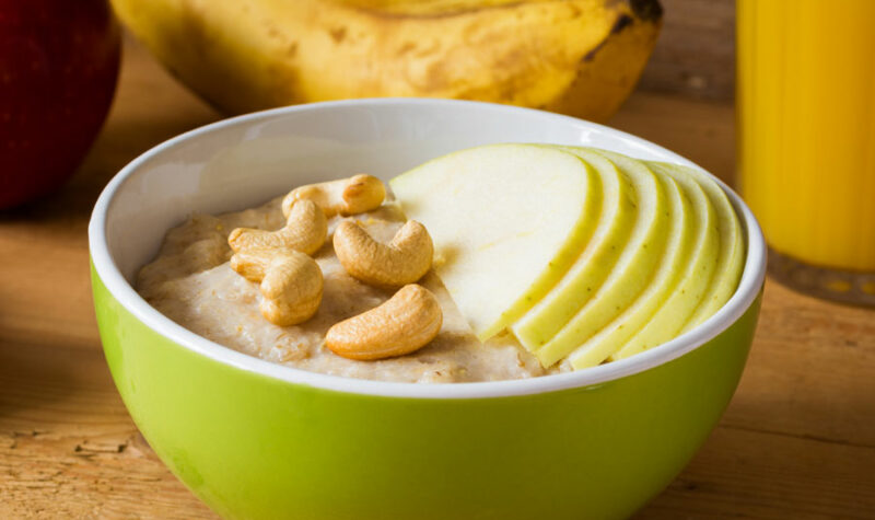 A bowl of oatmeal topped with cashews and apples