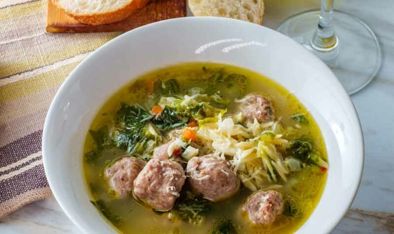 Italian wedding soup with meatballs in a white bowl.