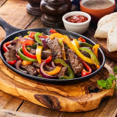 A cast iron skillet with steak fajitas and peppers.
