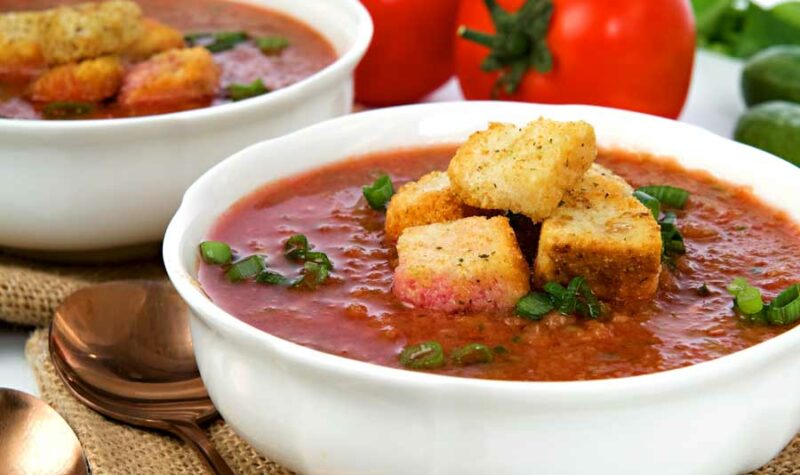 2 bowls of gazpacho with croutons on top.