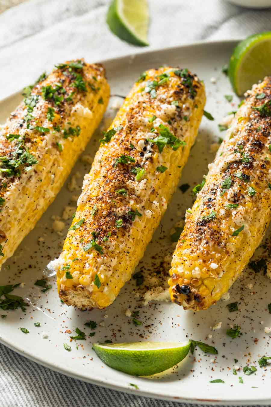 A plate of 3 ears of corn, covered in cheese and spices