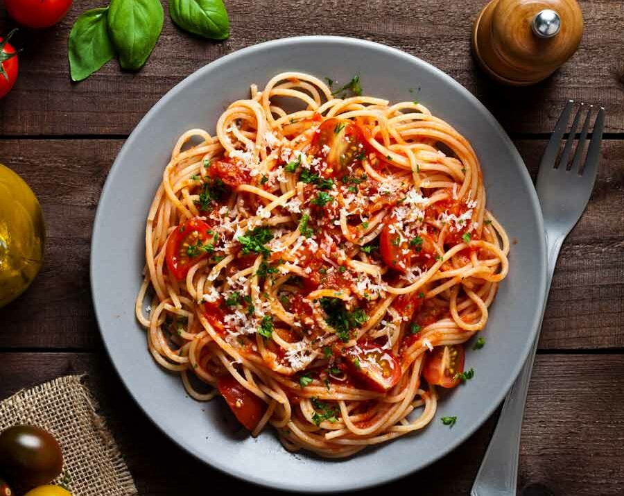 A gray plate filled with spaghetti, chopped fresh basil and parmesan.