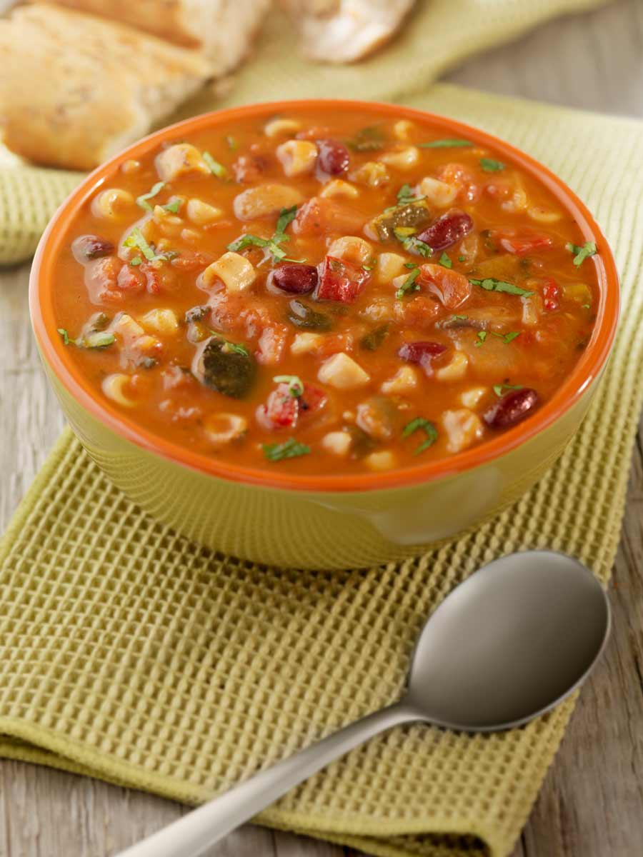 A bowl filled with minestrone soup and a spoon on the side.