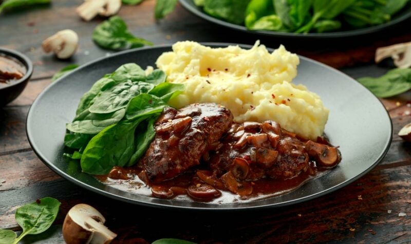 Cube steak on a plate with gravy, mashed potatoes and greens.