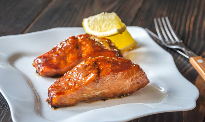 Marinated salmon on a plate with fresh lemon wedges in the background