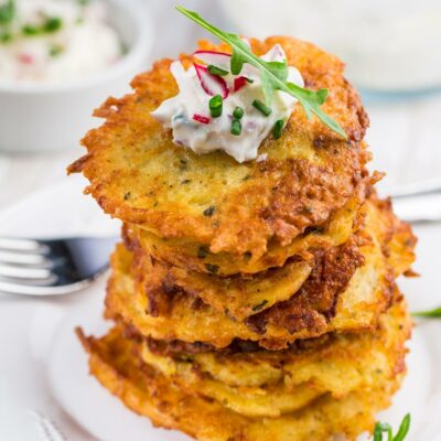 Potato pancakes stacked on a plate and topped with sour cream