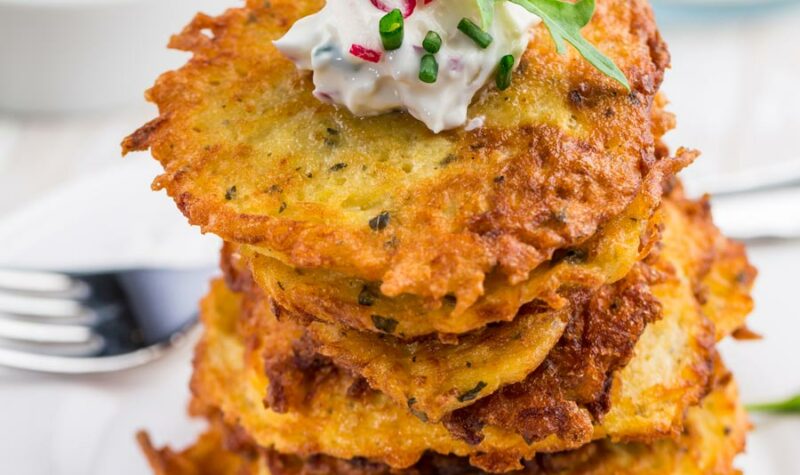 Potato pancakes stacked on a plate and topped with sour cream