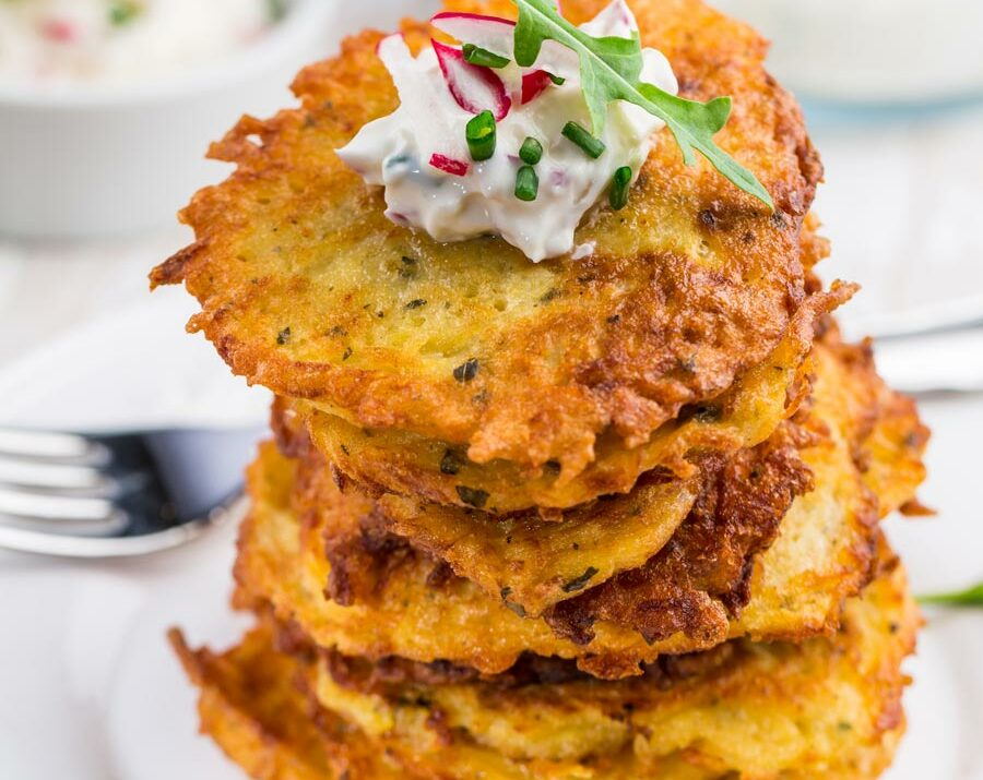 Potato pancakes stacked on a plate and topped with sour cream