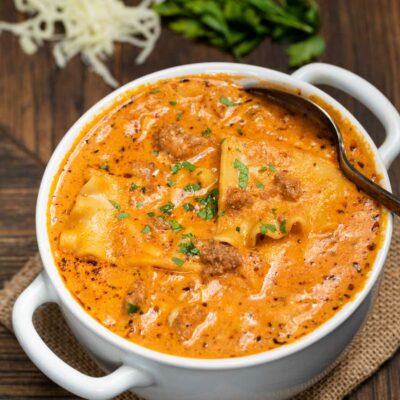 A white bowl filled with instant pot lasagna soup, with cheese and fresh parsley on the side.