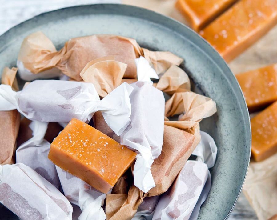 An overhead shot of a bowl of homemade caramel candies covered in wax paper.