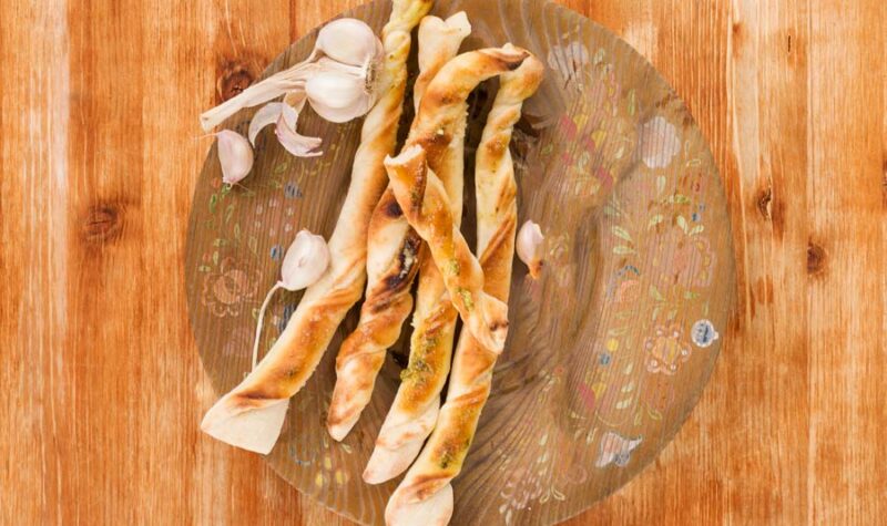 Breadsticks with garlic on wooden plate on wooden background, top view. Culinary pizzastick eating, rustic styles.