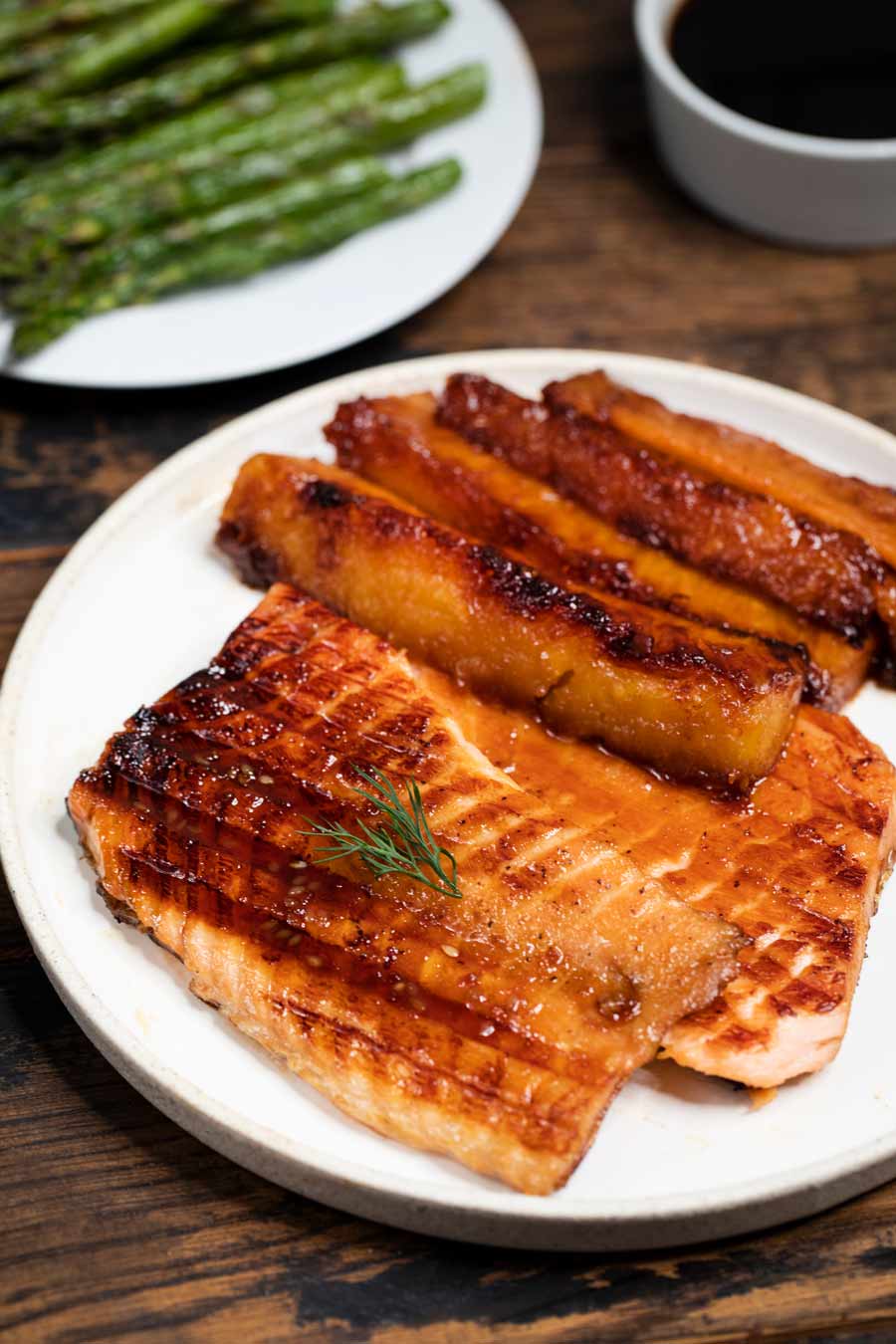 Grilled salmon and sugared grilled pineapple on a white plate with asparagus in the background.