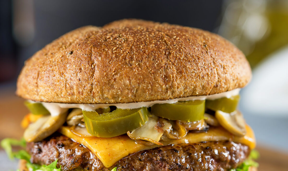 A beef burger topped with onions, jalapeno and cheese.