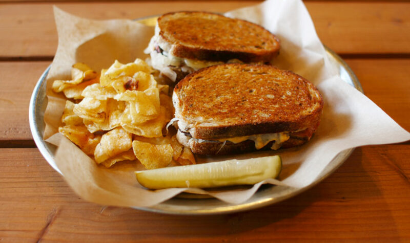 A vegan reuben sandwich on a plate with a side of chips.