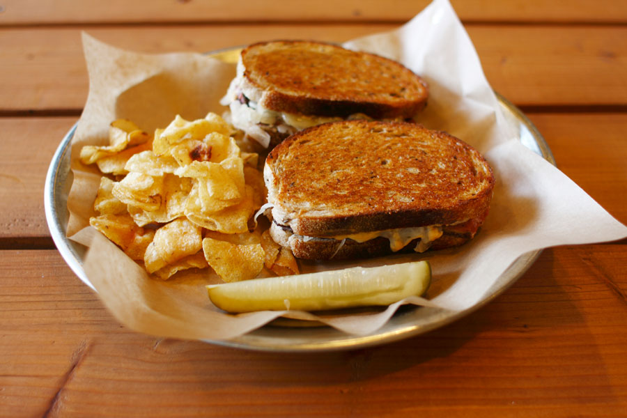 A vegan reuben sandwich on a plate with a side of chips.