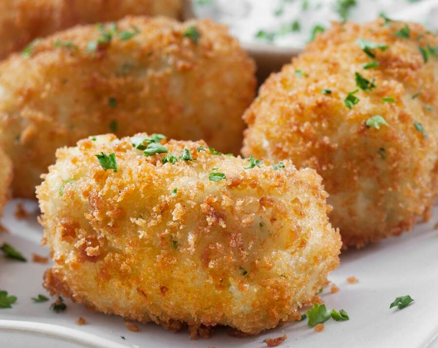 Fried mashed potato balls sprinkled with chives and a sauce on the side