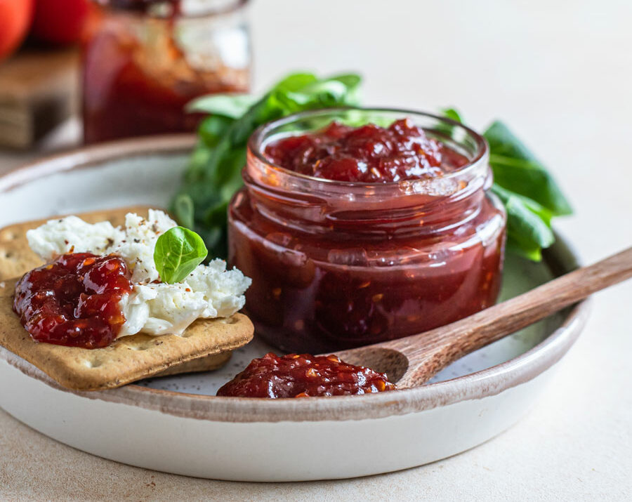 A jar of tomato jam with crackers on the side.
