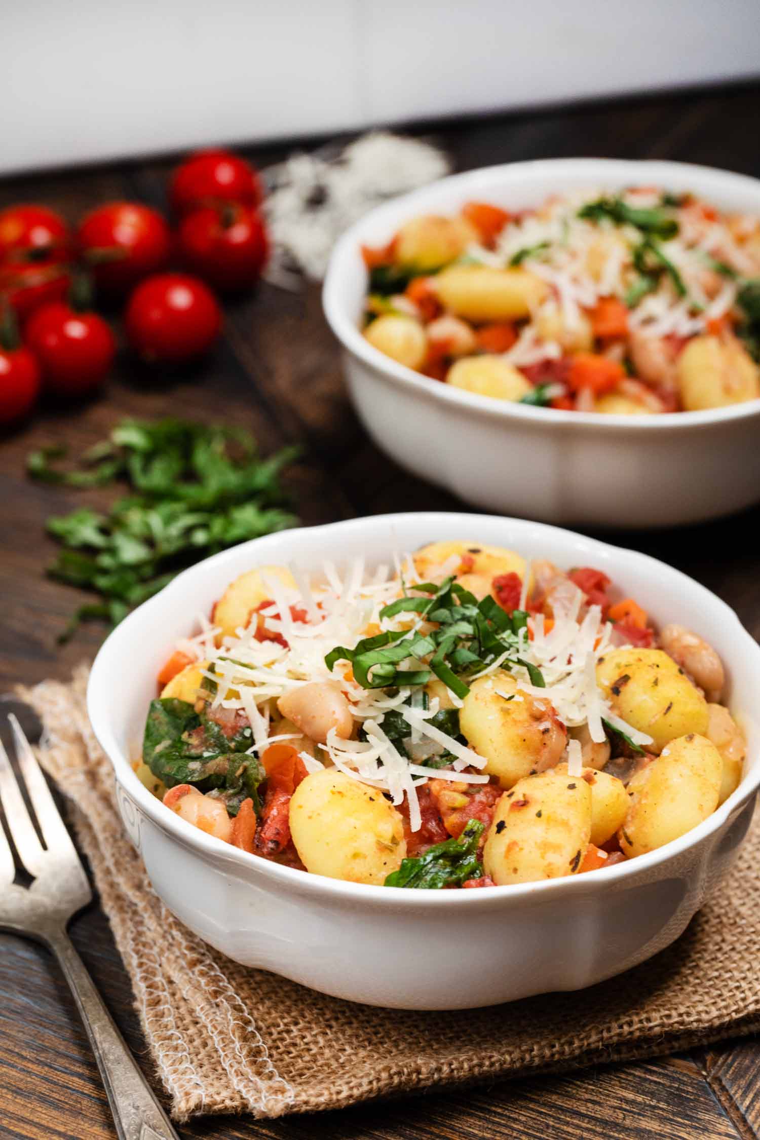 White Bean Gnocchi Skillet with tomatoes and vegan parmesan and basil on the side.