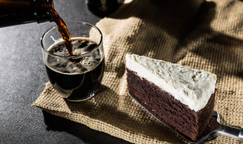 A piece of chocolate cake with beer being poured in the background.