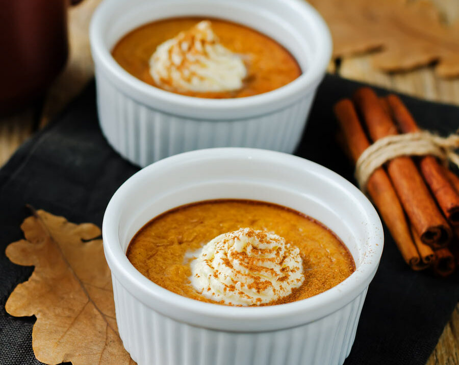 Two white bowls filled with pumpkin custard topped with whipped cream