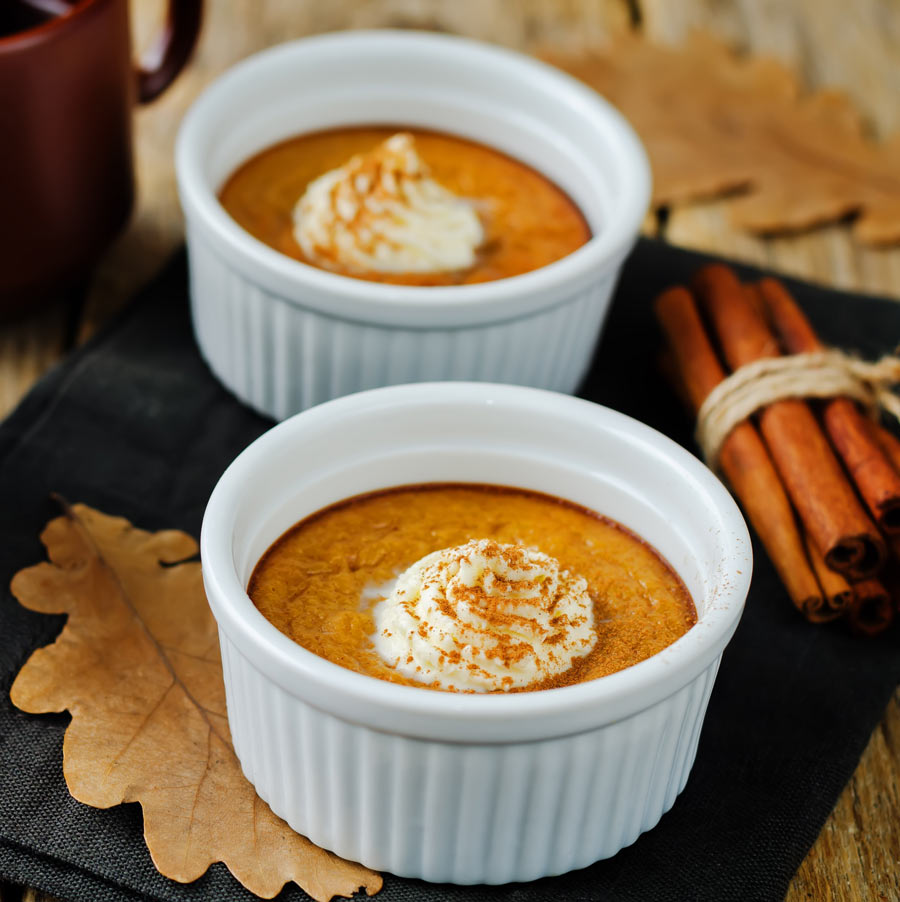 Two white bowls filled with pumpkin custard topped with whipped cream