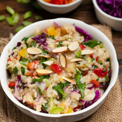 Colorful Asian Rice Salad in a white bowl with red pepper and red cabbage in the background.