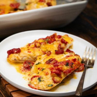 Cheesy chicken casserole w/ sundried tomatoes on a white plate.