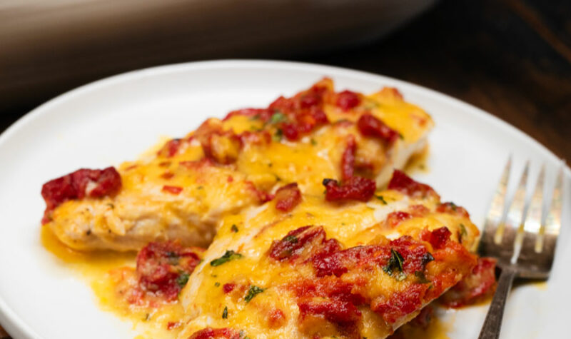 Cheesy chicken casserole w/ sundried tomatoes on a white plate.