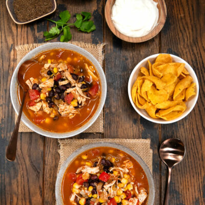 Easy chicken tortilla soup in 2 bowls with a side of chips and sour cream and cheese.