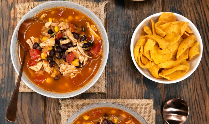 Easy chicken tortilla soup in 2 bowls with a side of chips and sour cream and cheese.