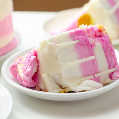 A slice of cake with pink frosting on a white plate - stock photo