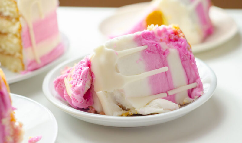 A slice of cake with pink frosting on a white plate - stock photo