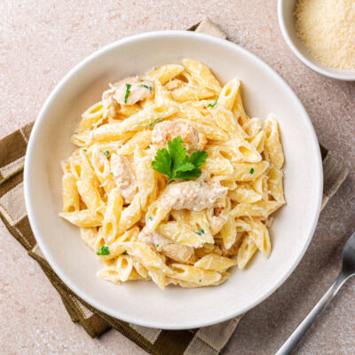 Creamy penne pasta in a white bowl with Parmesan cheese on the side