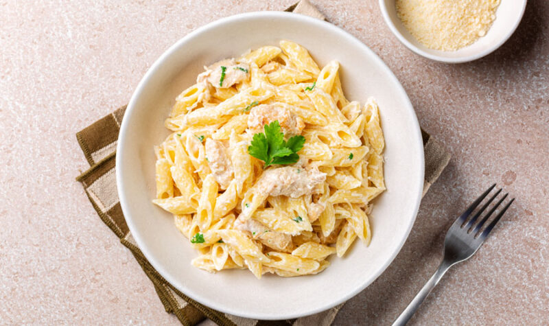 Creamy penne pasta in a white bowl with Parmesan cheese on the side