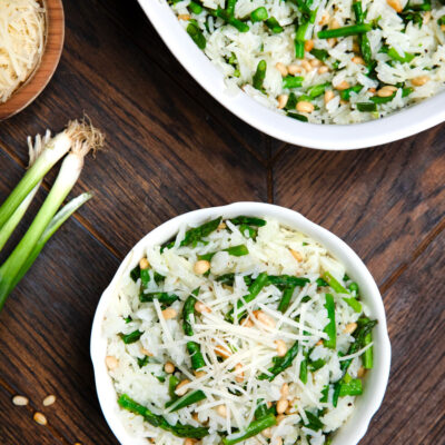 Asparagus rice salad in a white bowl w/ green onions on the side