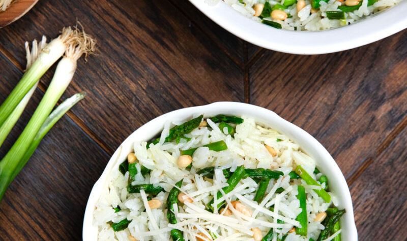 Asparagus rice salad in a white bowl w/ green onions on the side